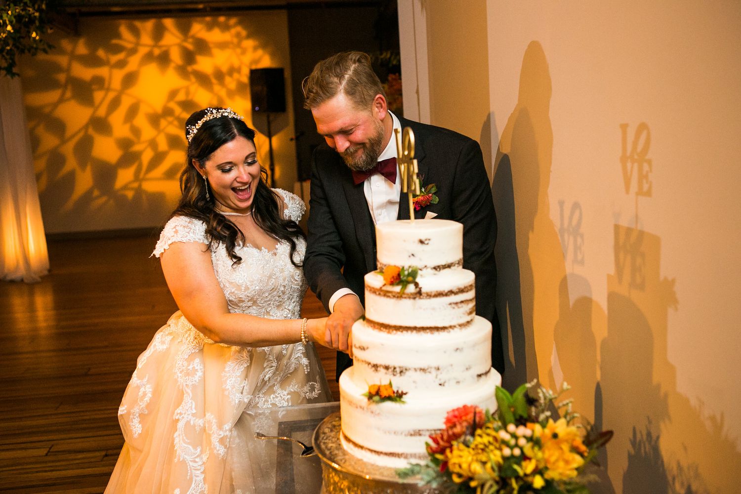Bride and groom smiling while cutting white semi-naked wedding cake at reception.
