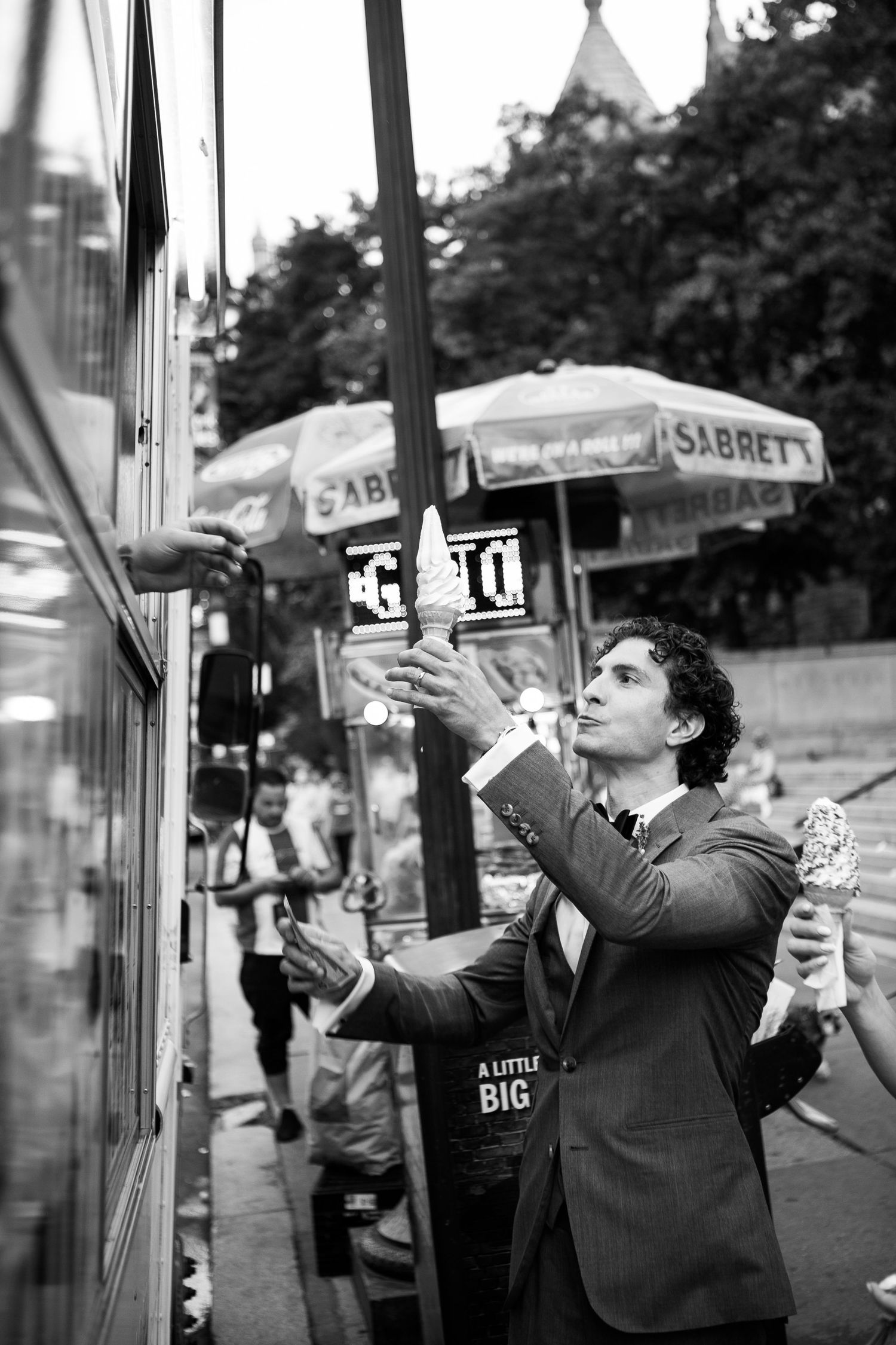 Black and white photo of a groom in a suit receiving ice cream cones from a street vendor truck.
