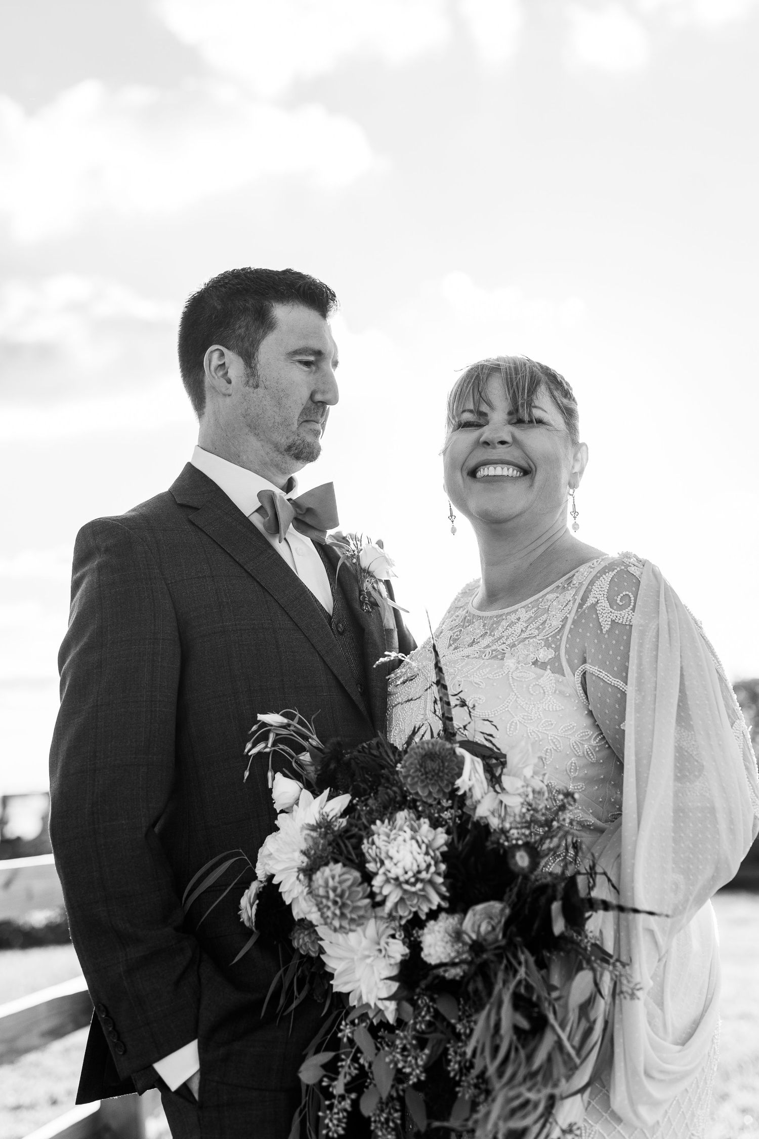 Black and white photo of smiling bride and groom holding bouquet on wedding day.