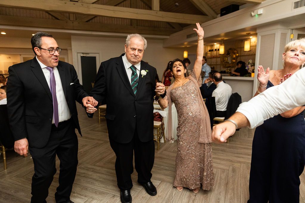 Elderly wedding guests dancing joyfully at indoor reception with warm lighting.