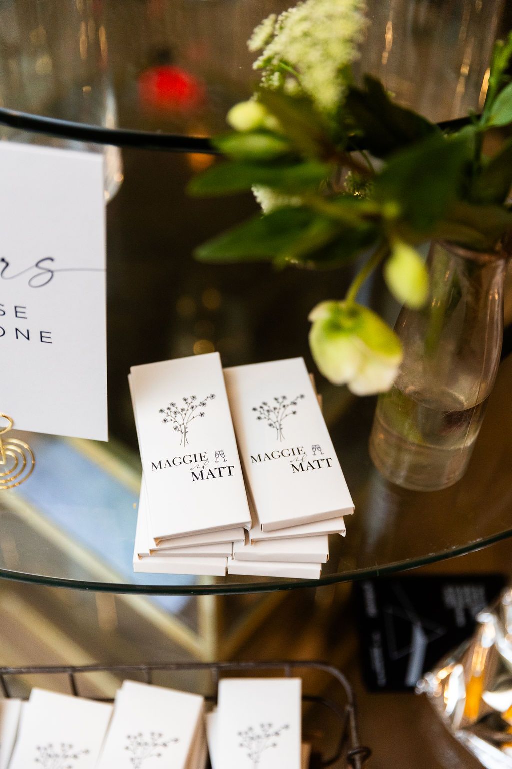 Wedding programs for Maggie and Matt displayed on glass table with floral arrangement.