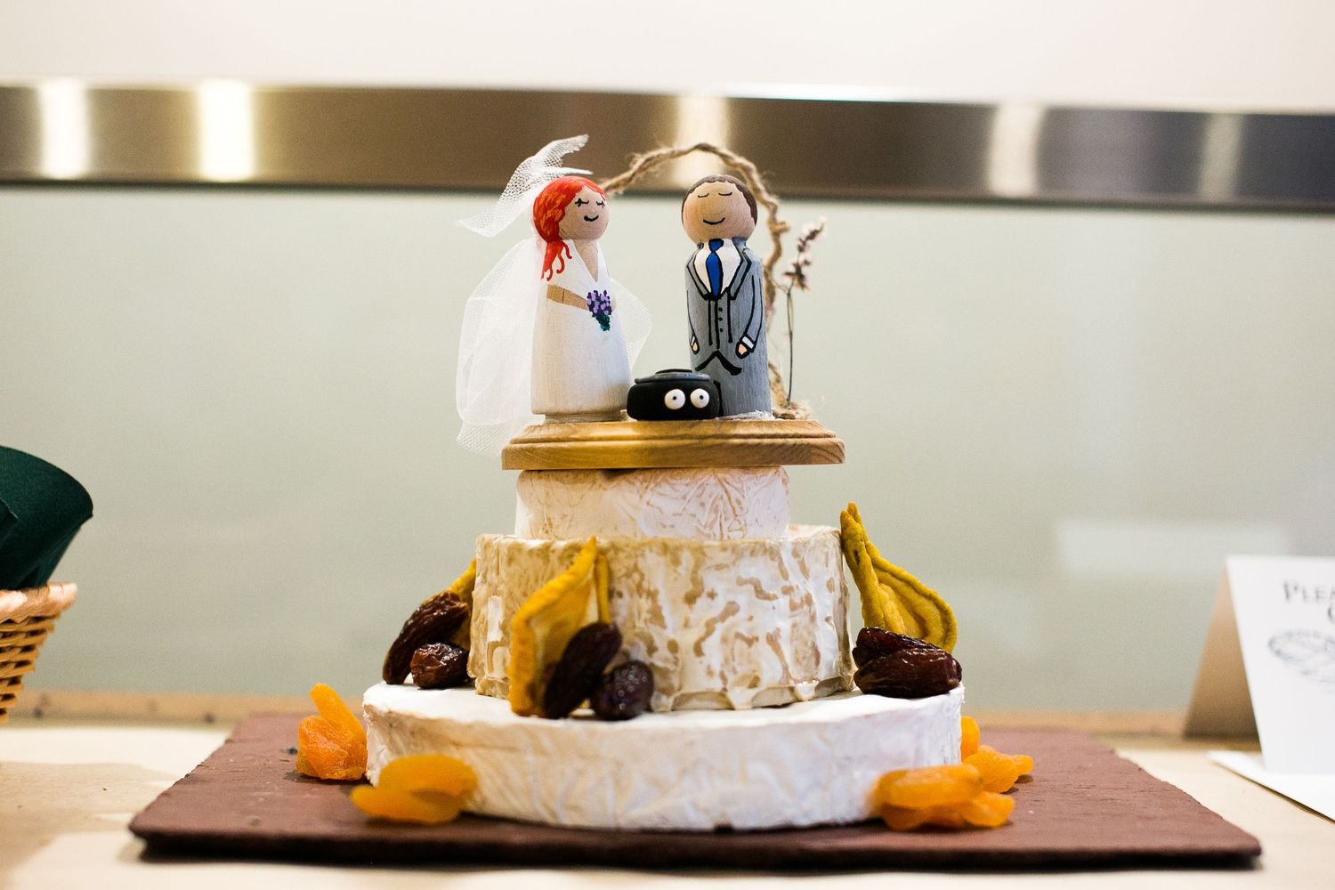 Unique wedding cake topped with custom bride and groom figurines on a rustic cheese wheel base.