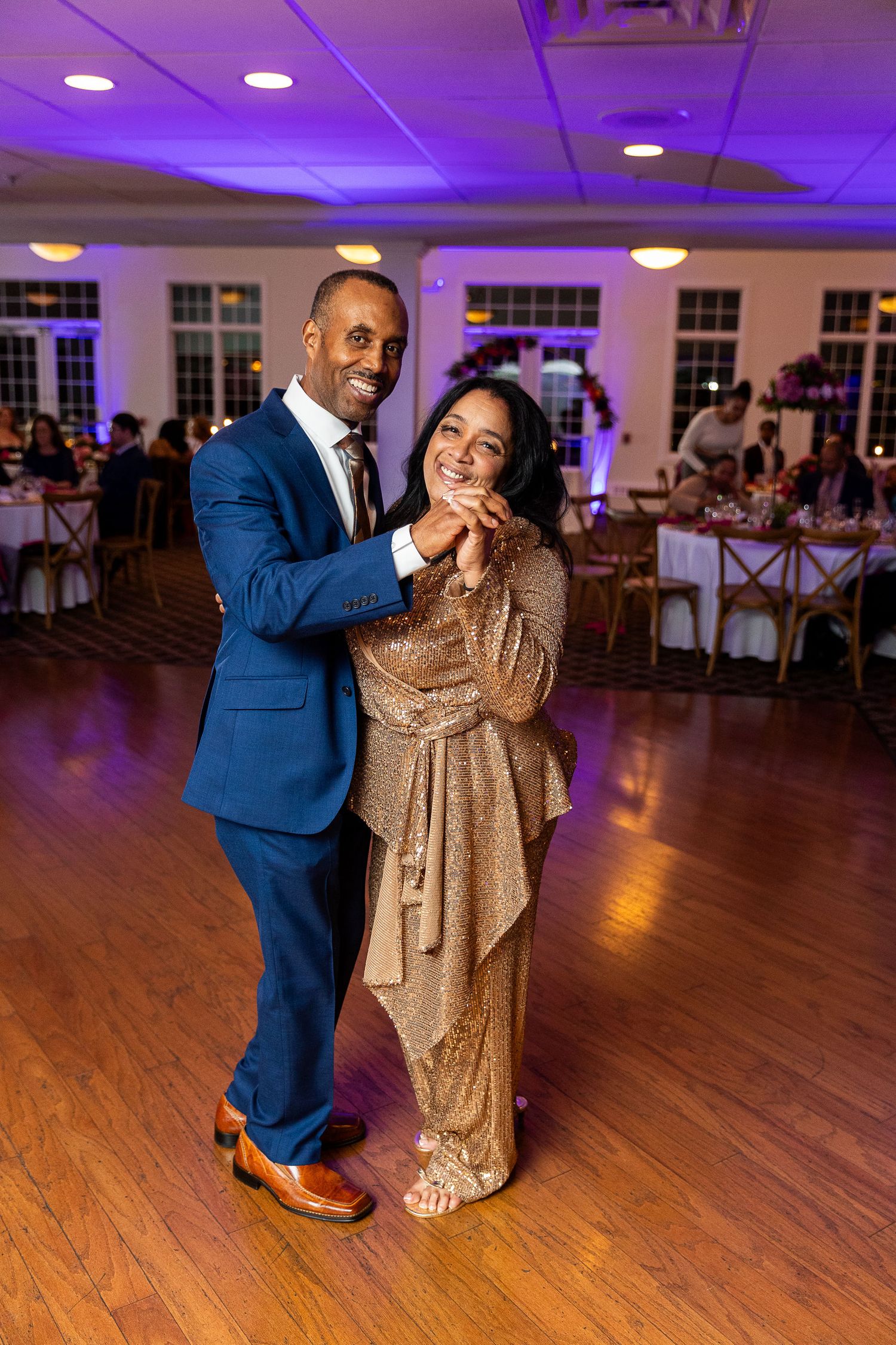Couple dancing elegantly on wedding reception dance floor with purple ambient lighting backdrop.