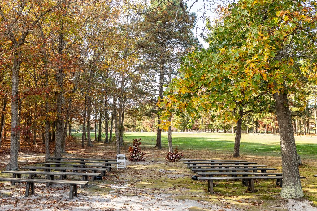 Outdoor wedding ceremony venue with wooden benches arranged among colorful autumn trees in a park setting.