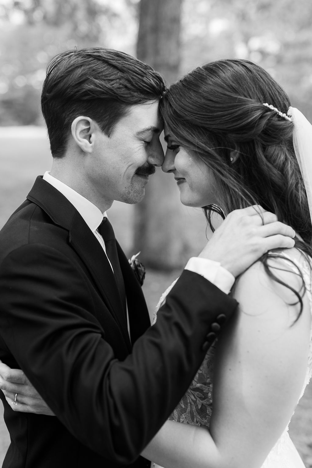 Black and white romantic portrait of bride and groom touching foreheads in tender embrace.