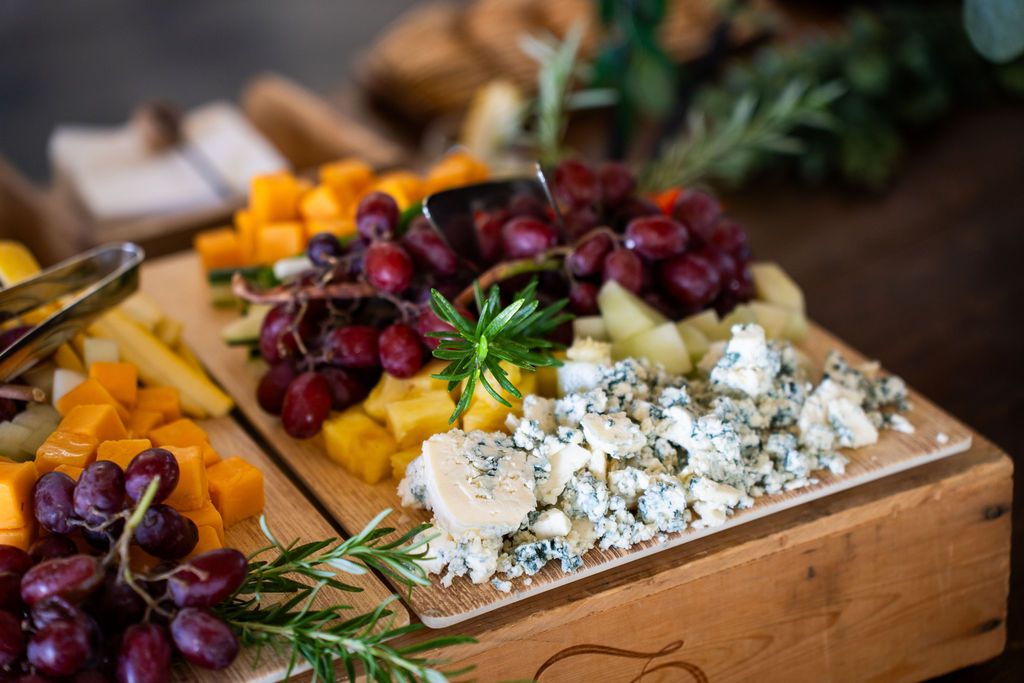 Elegant wedding charcuterie board with grapes, cheese, and fresh herbs on a wooden platter.