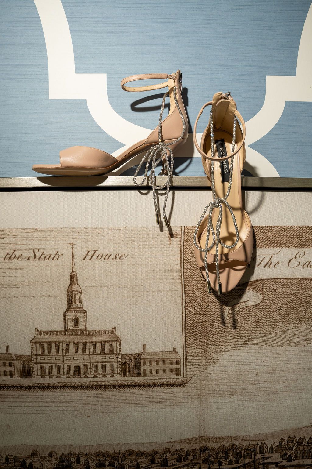 Nude strappy bridal heels displayed on a surface featuring an engraving of the State House.