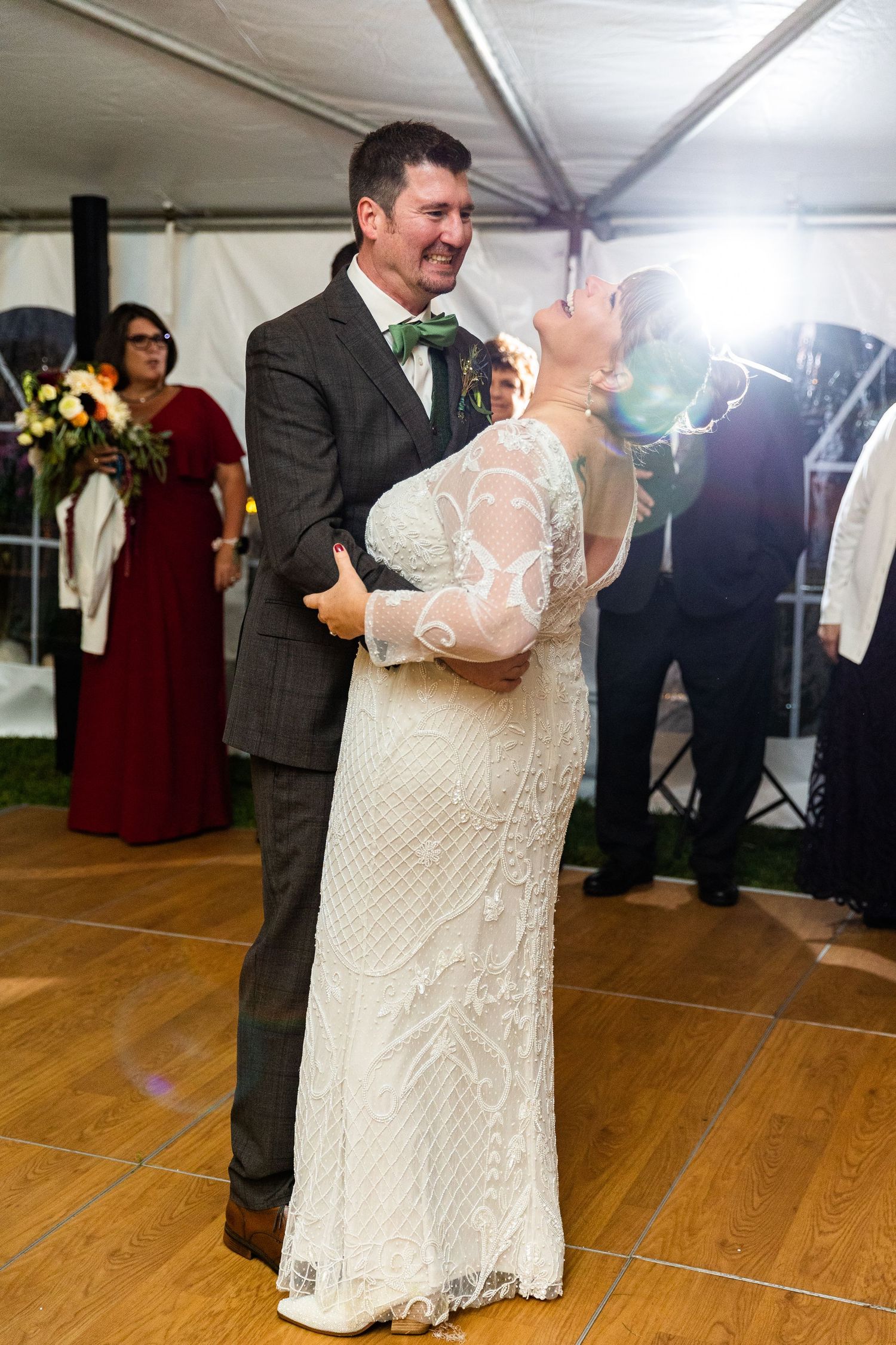 Bride and groom smiling during first dance at elegant tent wedding reception with string lights.