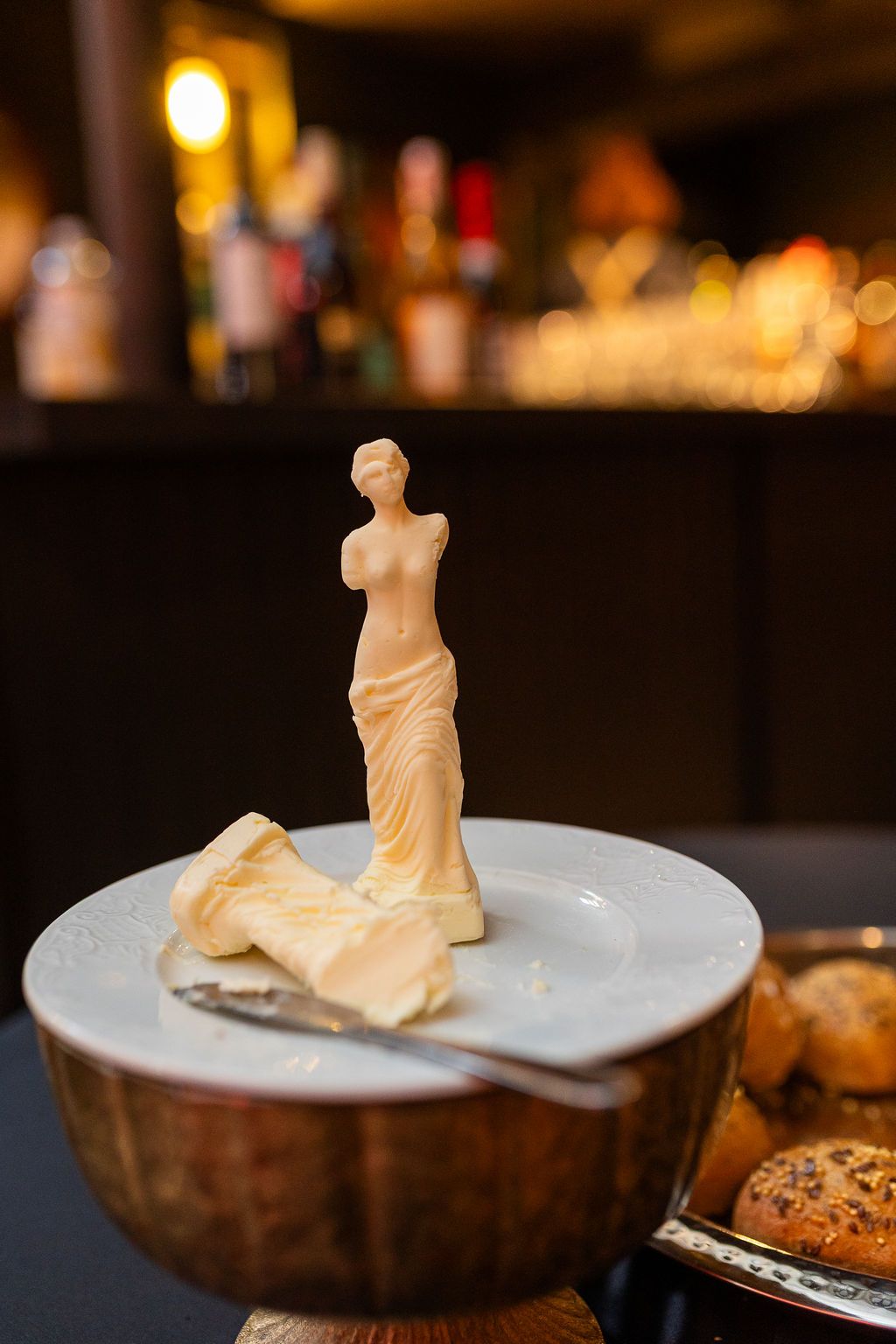 Elegant butter sculpture of Venus de Milo statue on a white plate at a restaurant.