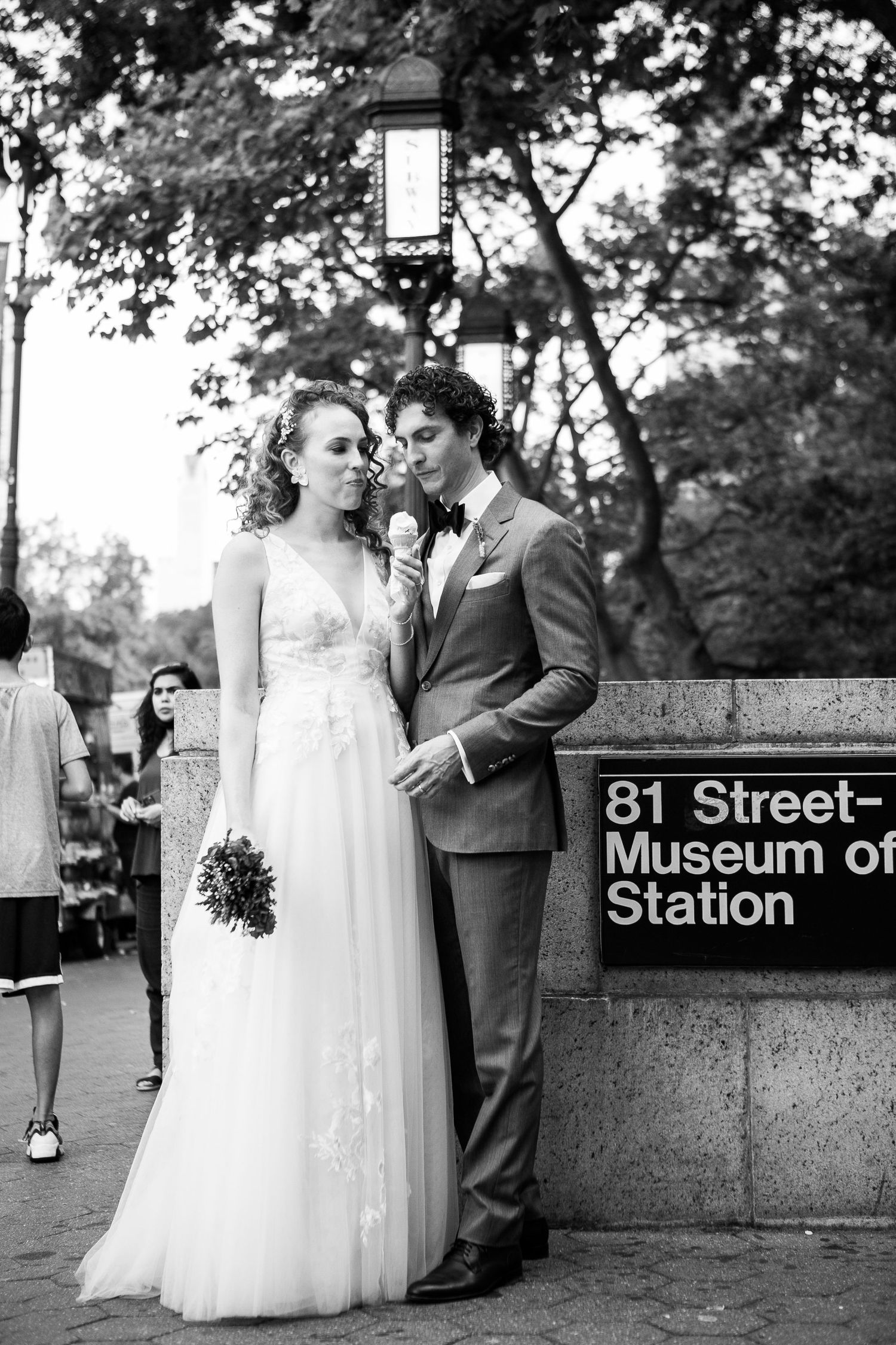 Black and white photo of newlyweds posing by the 81st Street Museum of Natural History subway station sign.