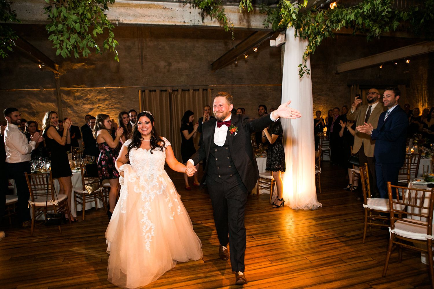 Bride in white gown and groom in black tuxedo make grand entrance at elegant wedding reception.