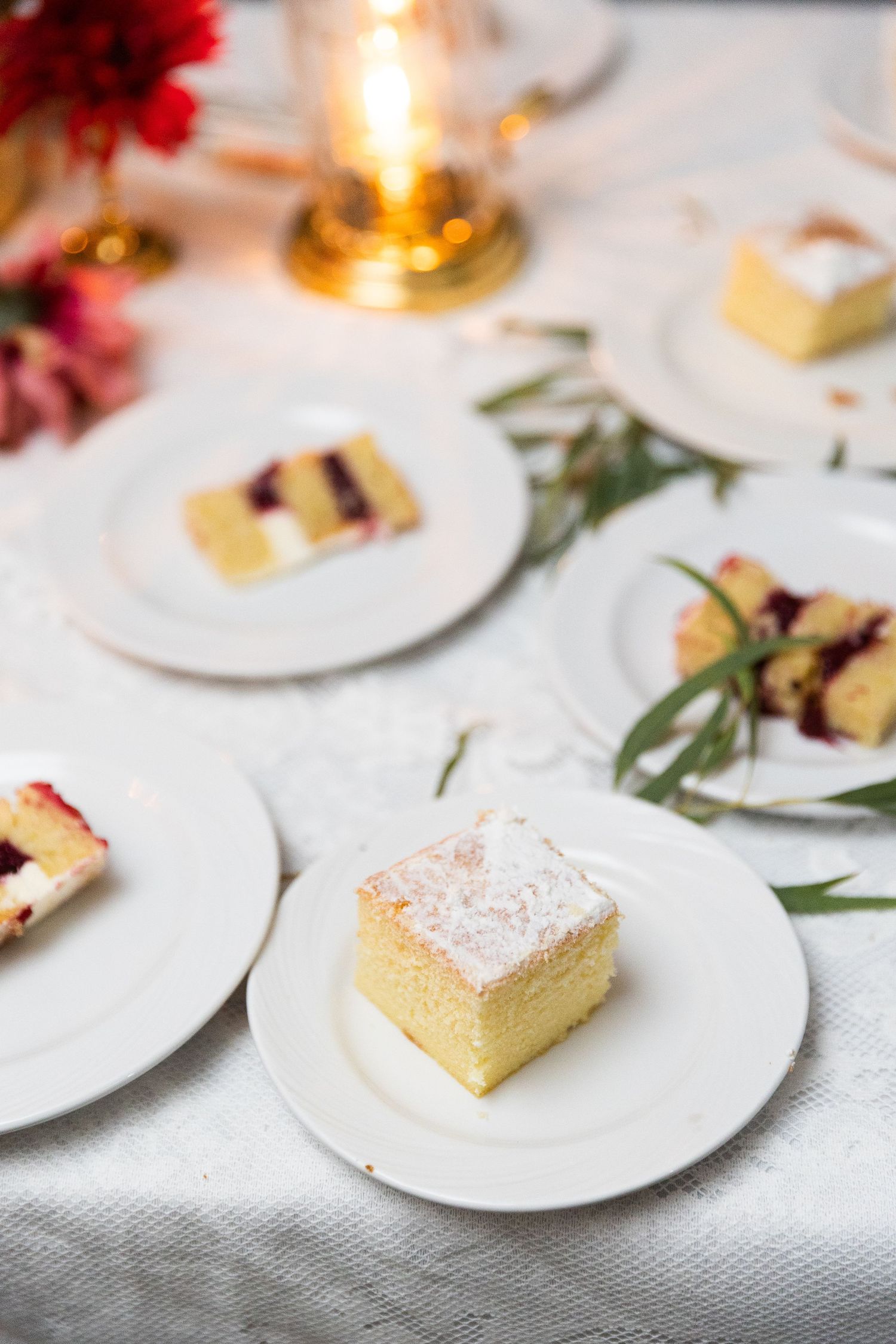 Elegant wedding cake slices with powdered sugar on white plates with candle centerpiece.