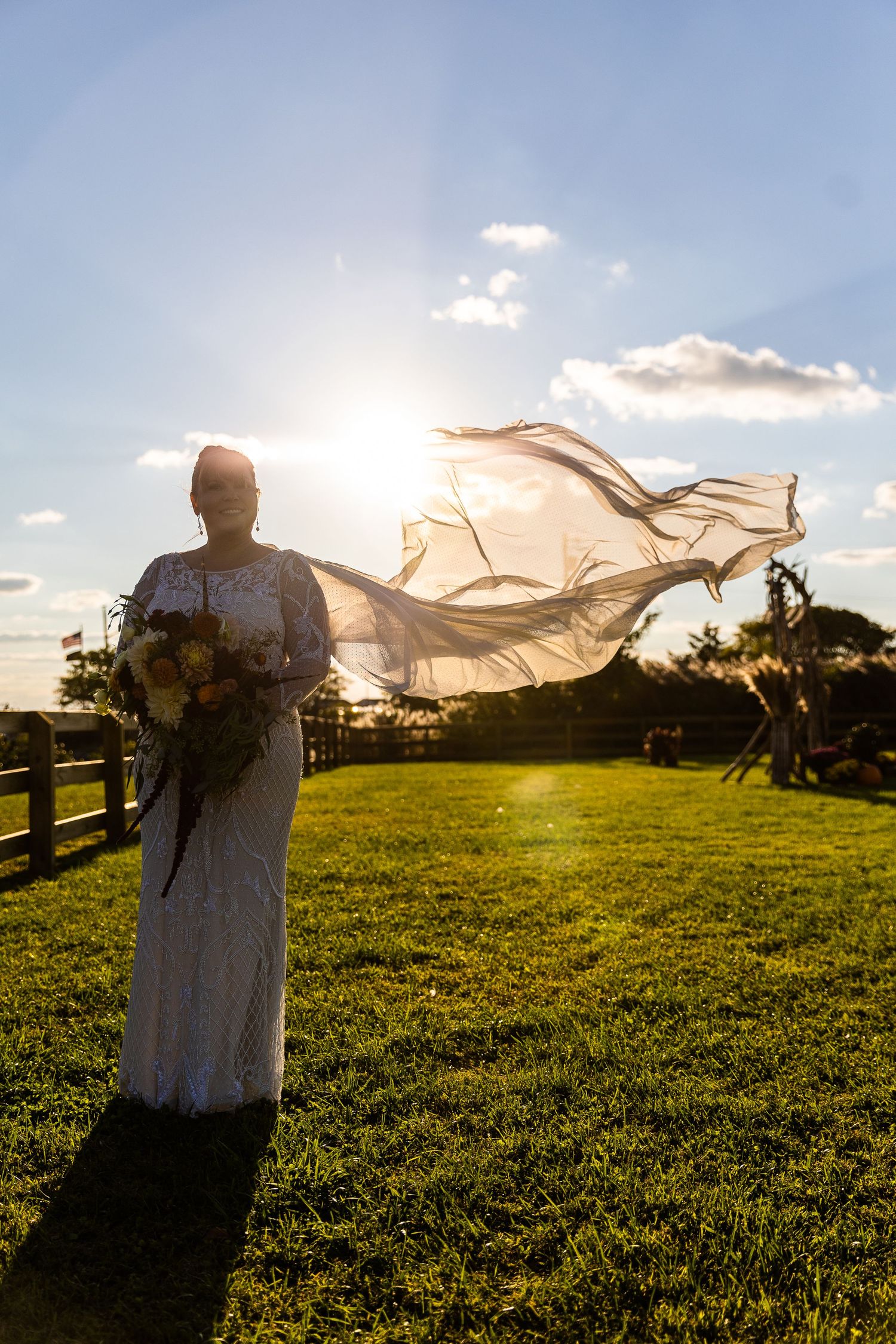 Bride standing in golden sunlight with veil dramatically flowing in the breeze.