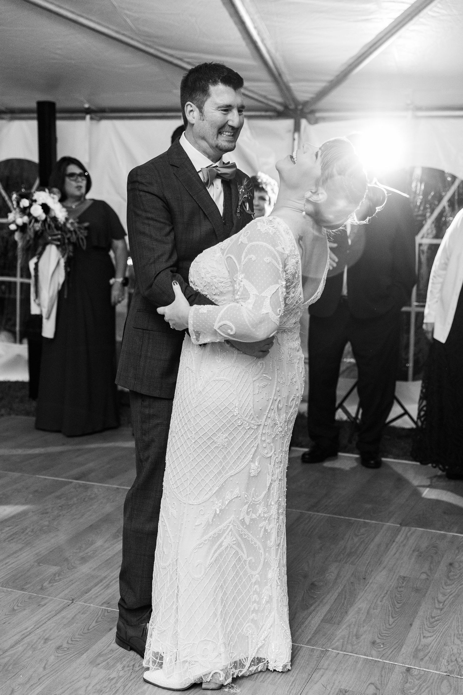 Black and white photo of bride and groom sharing first dance at wedding reception under tent.