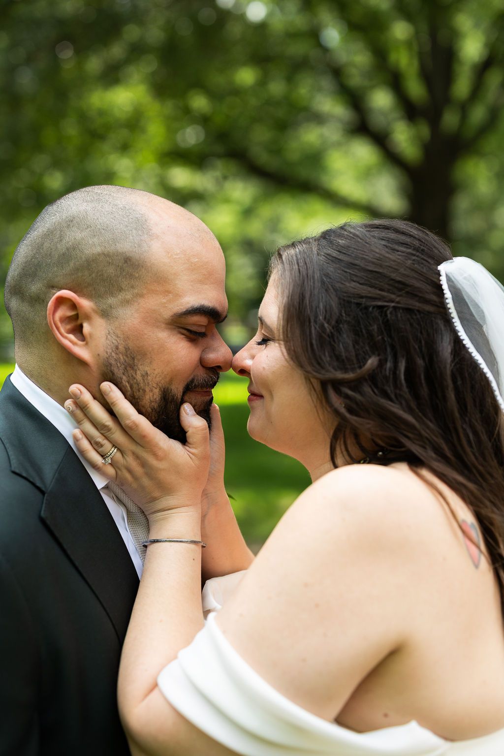 Close-up of smiling bride and groom nearly kissing, bride gently holding grooms face in her hands.