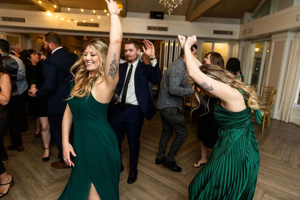 Guests in emerald green dresses dance joyfully with a man in a suit at a lively wedding reception.