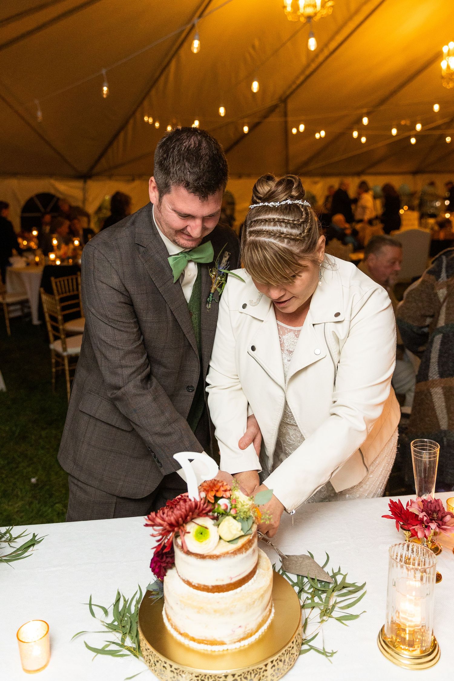 Bride and groom cut their rustic naked wedding cake at their tented outdoor reception.