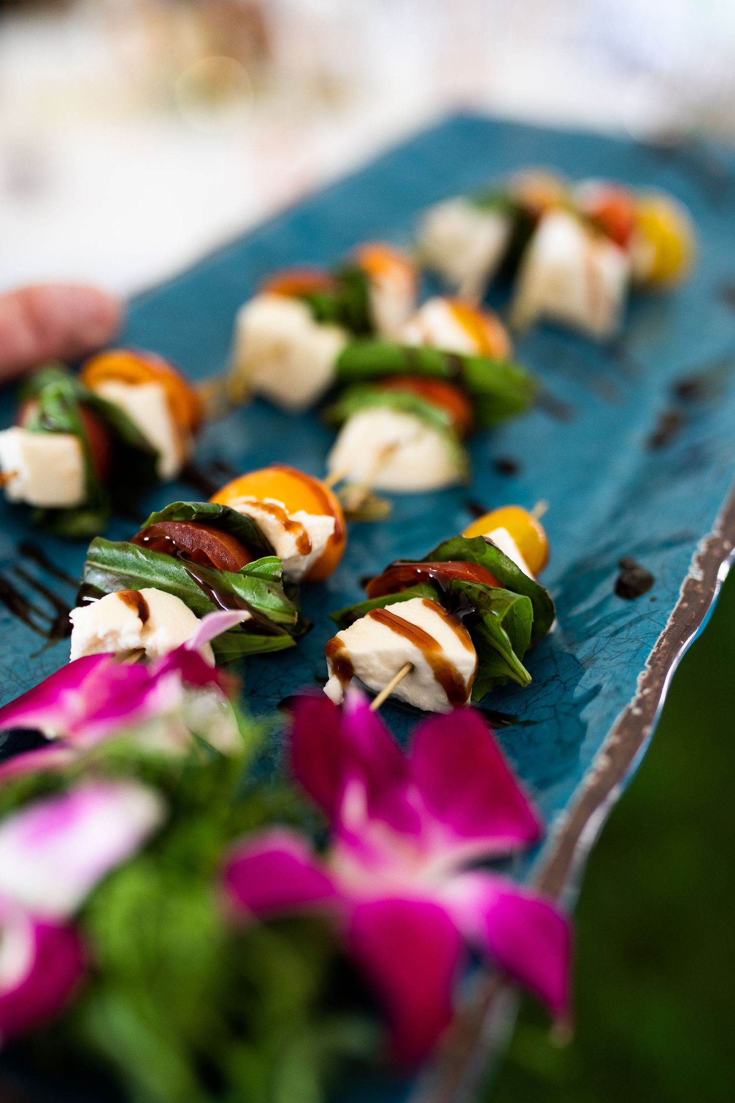 Elegant caprese skewer appetizers with mozzarella, tomatoes, and basil on a teal slate platter with orchids.