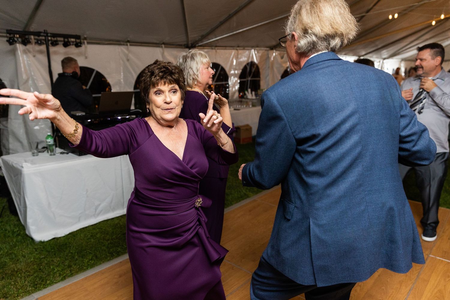 Woman in purple dress dances joyfully with partner at lively outdoor tented wedding reception.