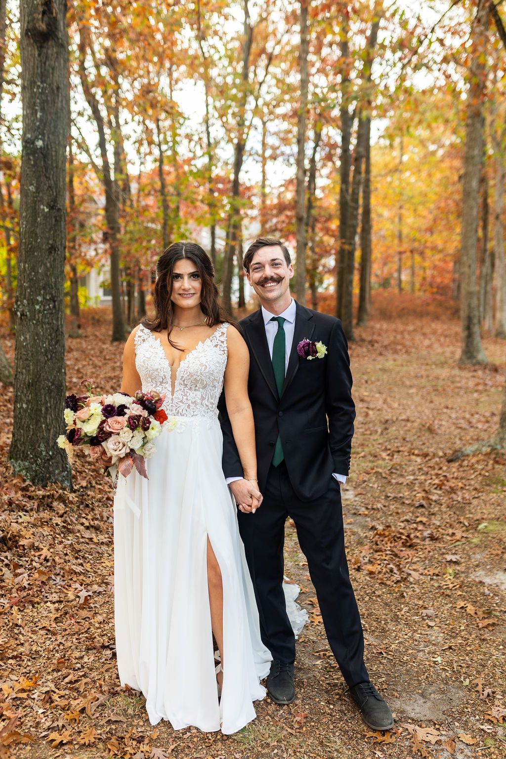 Bride and groom holding hands in autumn forest, groom wearing green tie.