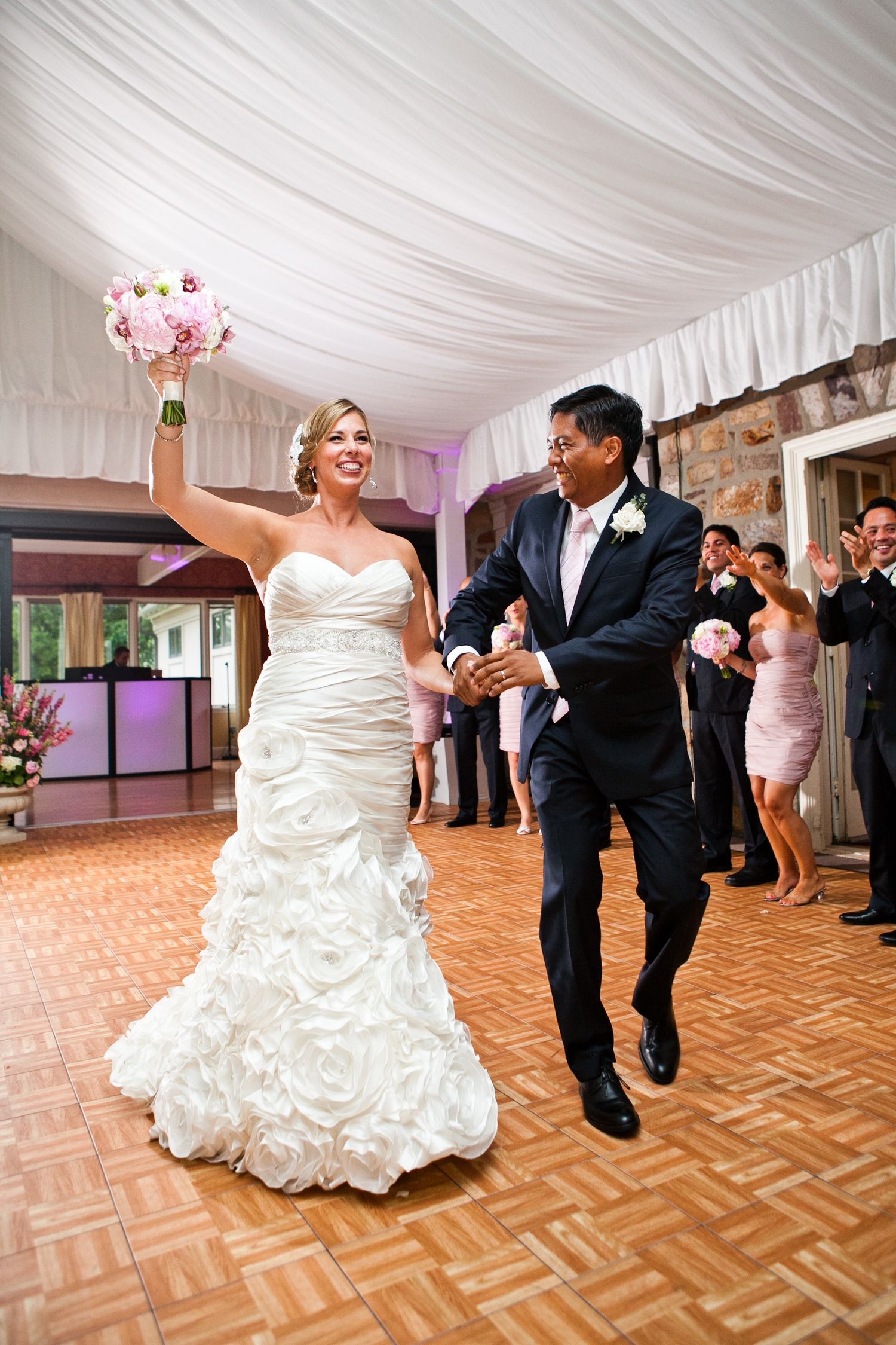 Bride raising bouquet as couple makes grand entrance at wedding reception.