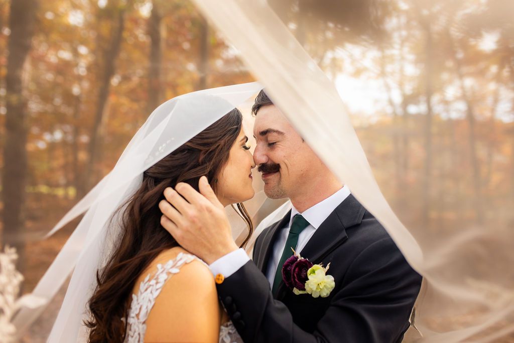 Newlyweds kiss tenderly beneath a bridal veil surrounded by colorful autumn foliage.