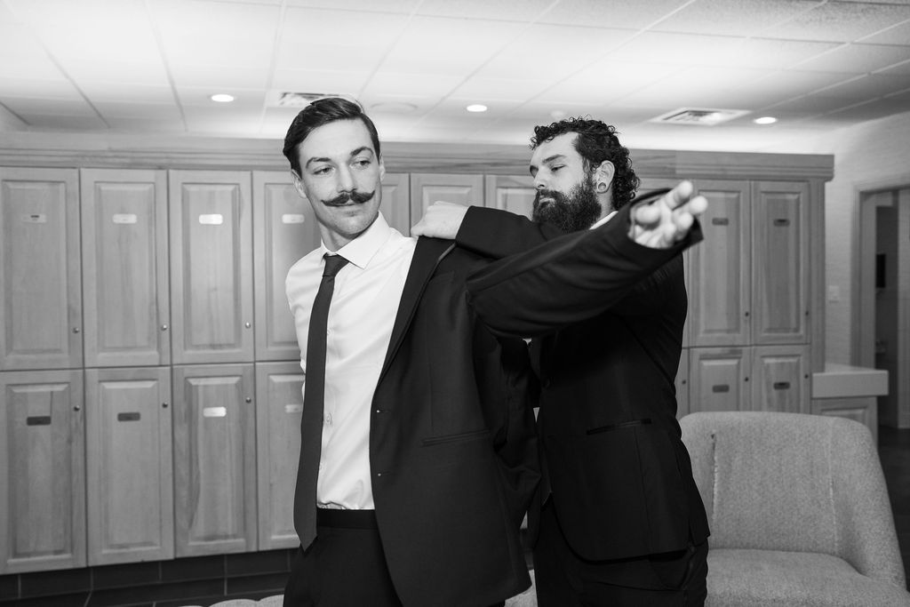 Black and white photo of two groomsmen joking around in a locker room before a wedding.