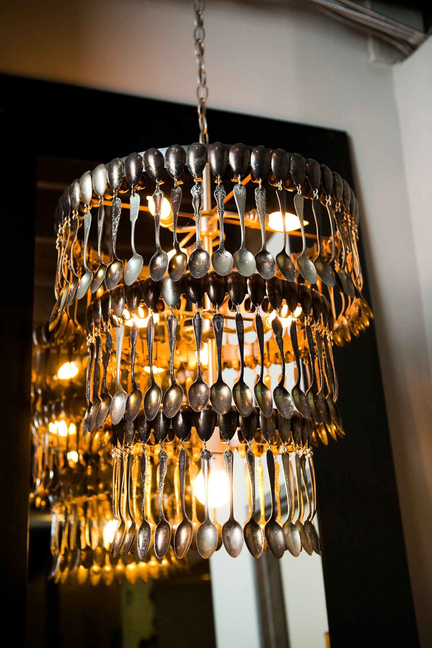 Unique tiered chandelier made entirely of silver spoons glowing warmly in a wedding venue.