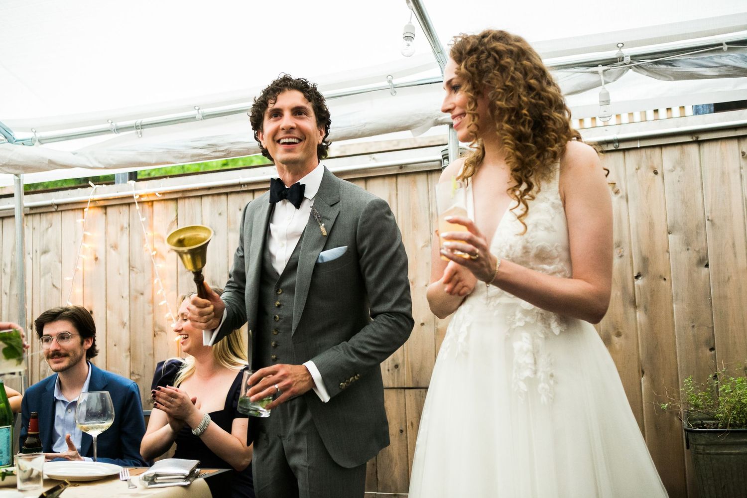 Bride and groom laughing during wedding reception toast in outdoor venue.