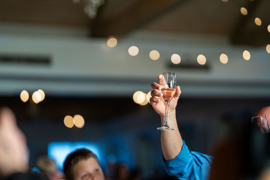 Guest raises champagne glass for a toast at elegant wedding reception with bokeh lights background.