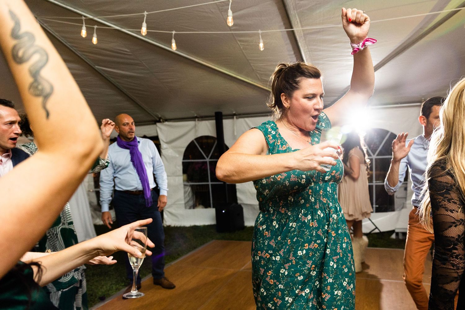 Woman in green floral dress dancing energetically at a lively wedding reception party.