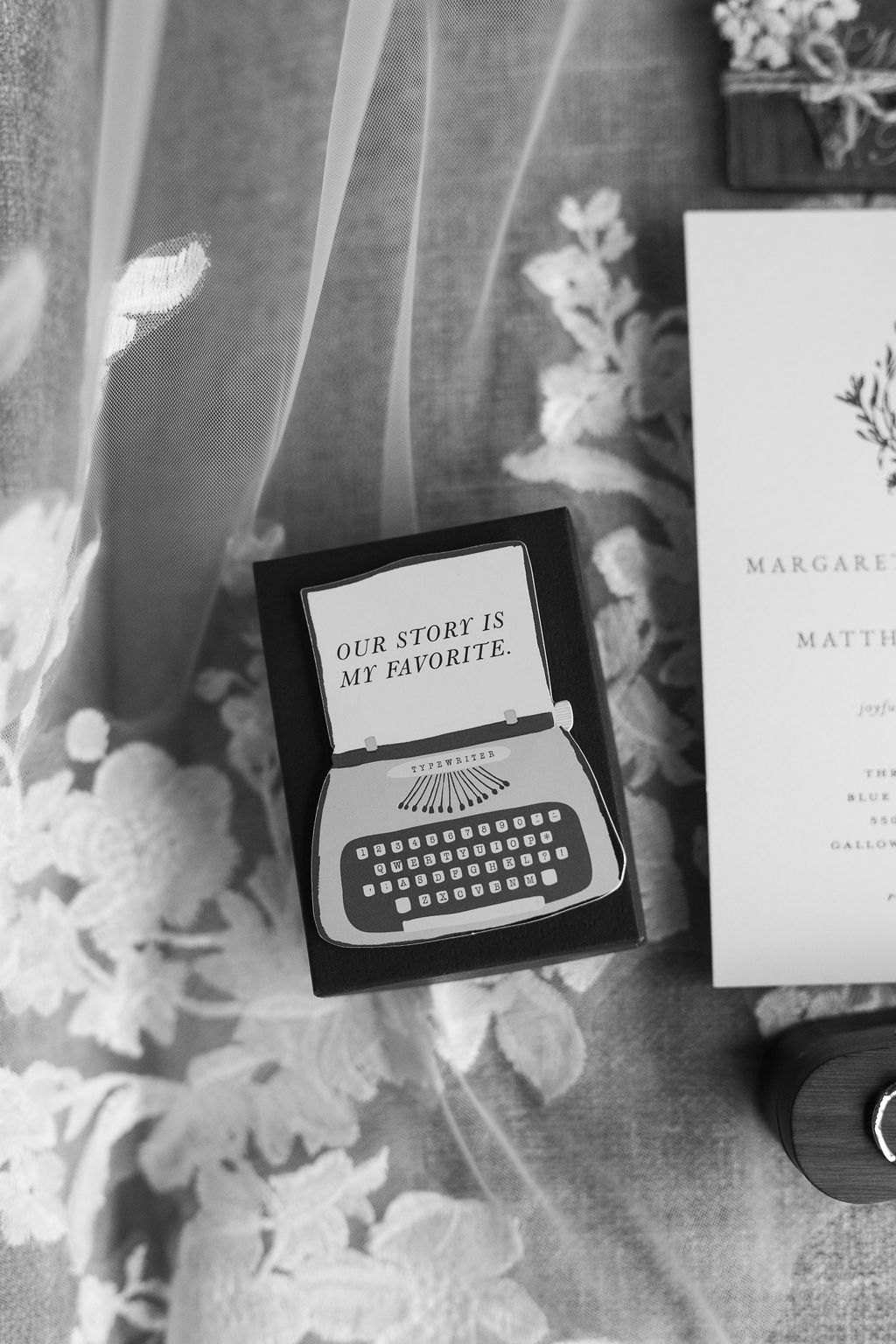 Black and white flat lay of a typewriter-themed card reading Our Story Is My Favorite beside wedding stationery.