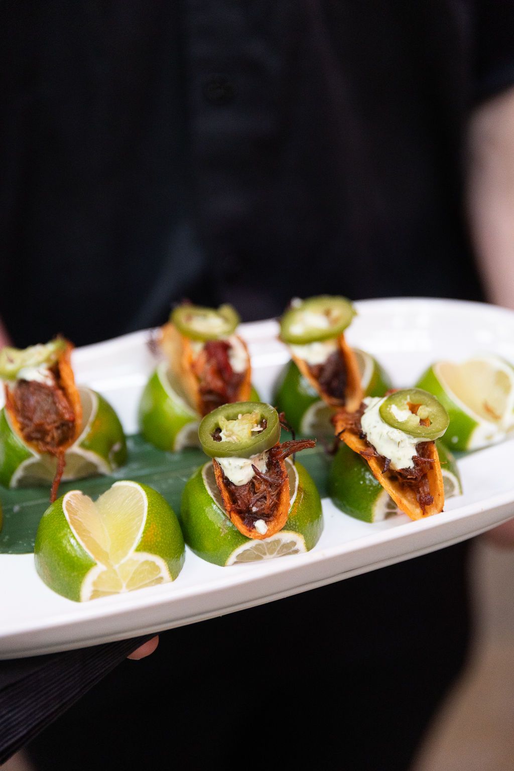 Server presents an elegant platter of mini tacos garnished with jalapenos and lime wedges.