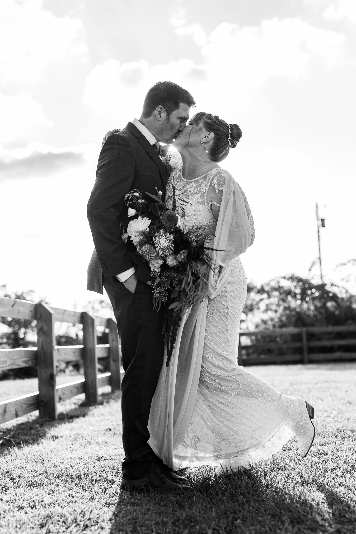 Black and white photo of bride and groom kissing outdoors, bride holding a large floral bouquet.