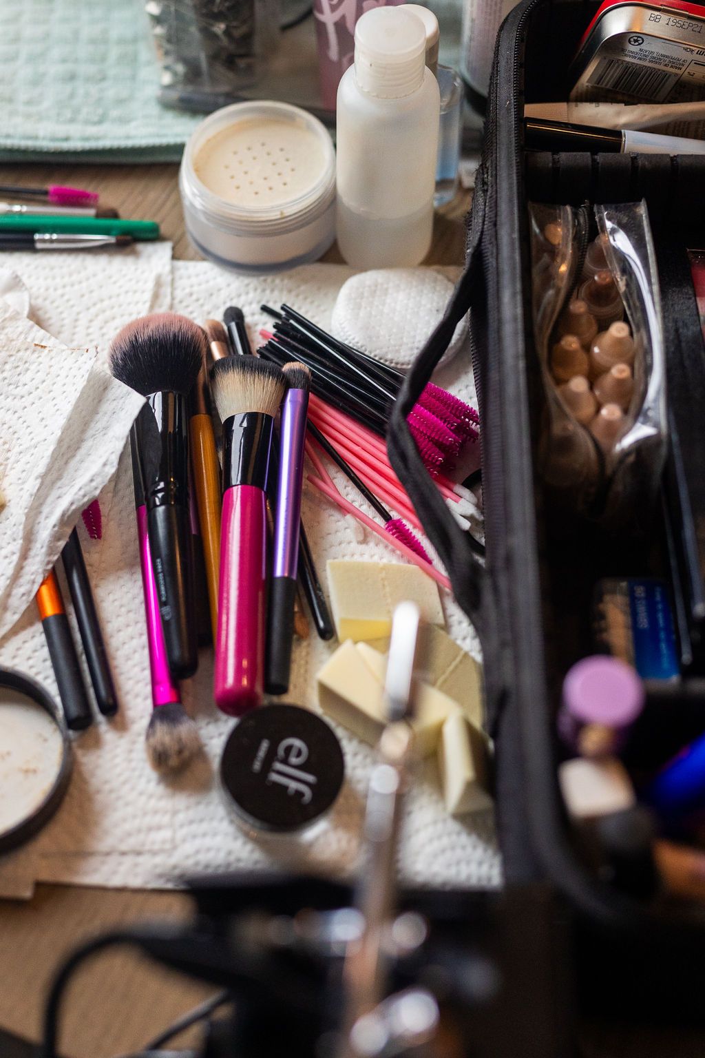 Assorted makeup brushes, ELF compact, and beauty products spread on a white cloth beside an open cosmetic case.