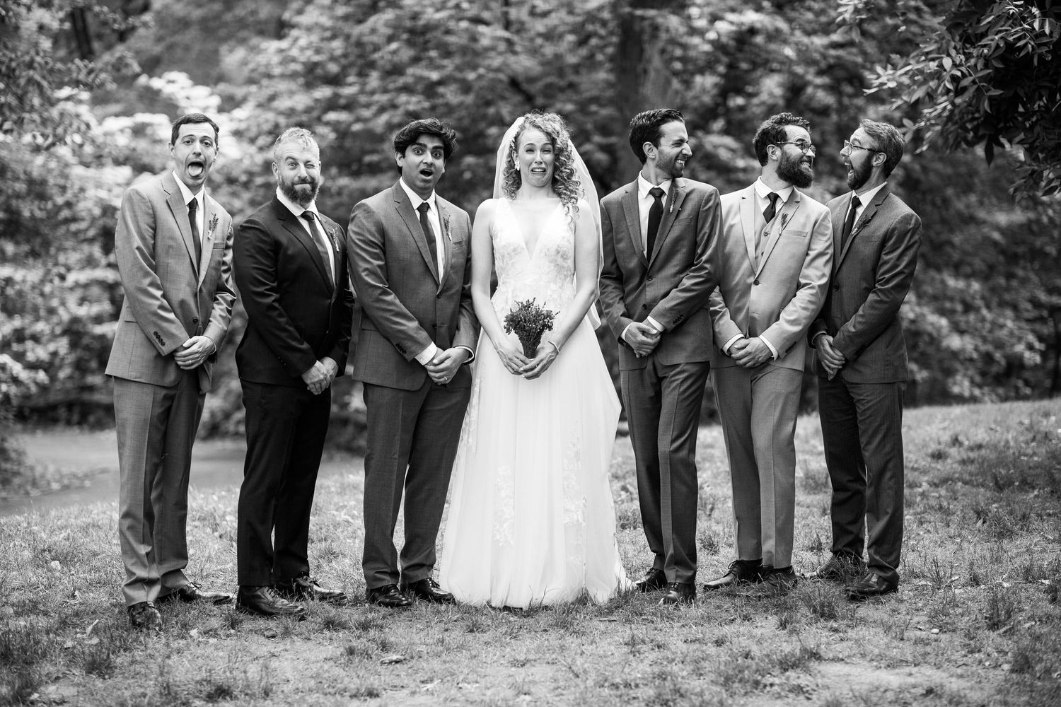 Black and white photo of bride posing with groomsmen in suits outdoors.