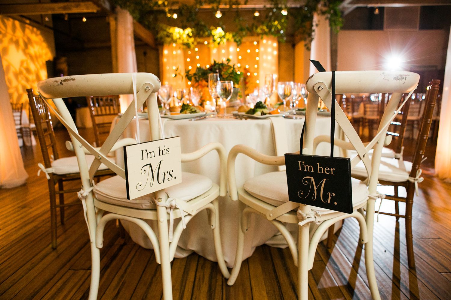 Bride and groom sweetheart table chairs with Mr. and Mrs. signs at wedding reception.