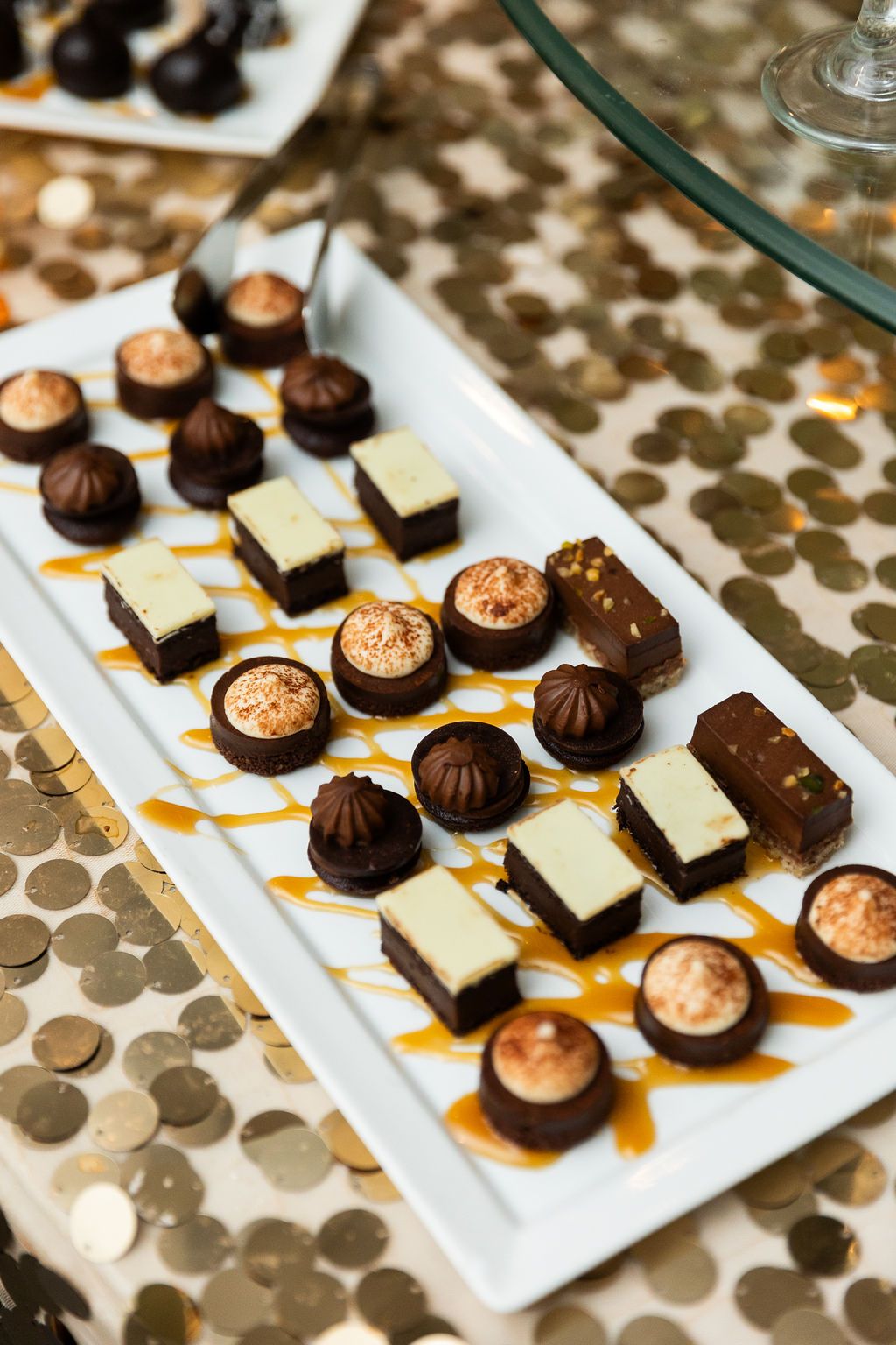 Assorted chocolate truffles and desserts with caramel drizzle on white platter at wedding.