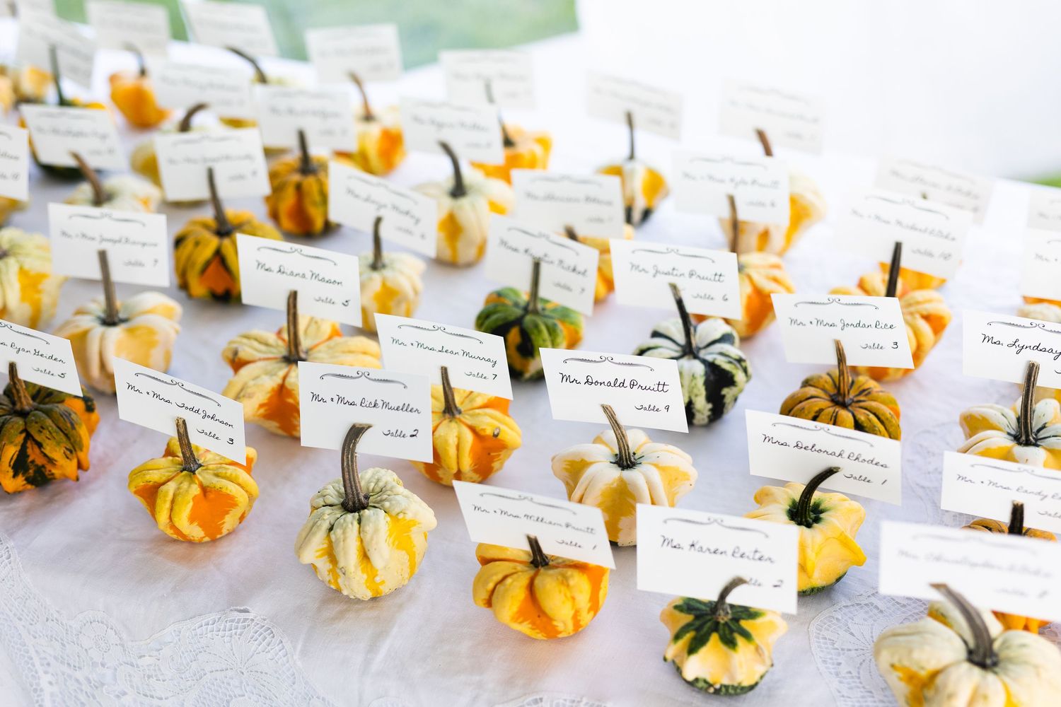 Small decorative yellow and orange gourds used as place card holders on wedding reception table.