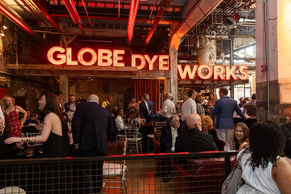 Guests mingling at Globe Dye Works venue under glowing red neon sign during an upscale social event.
