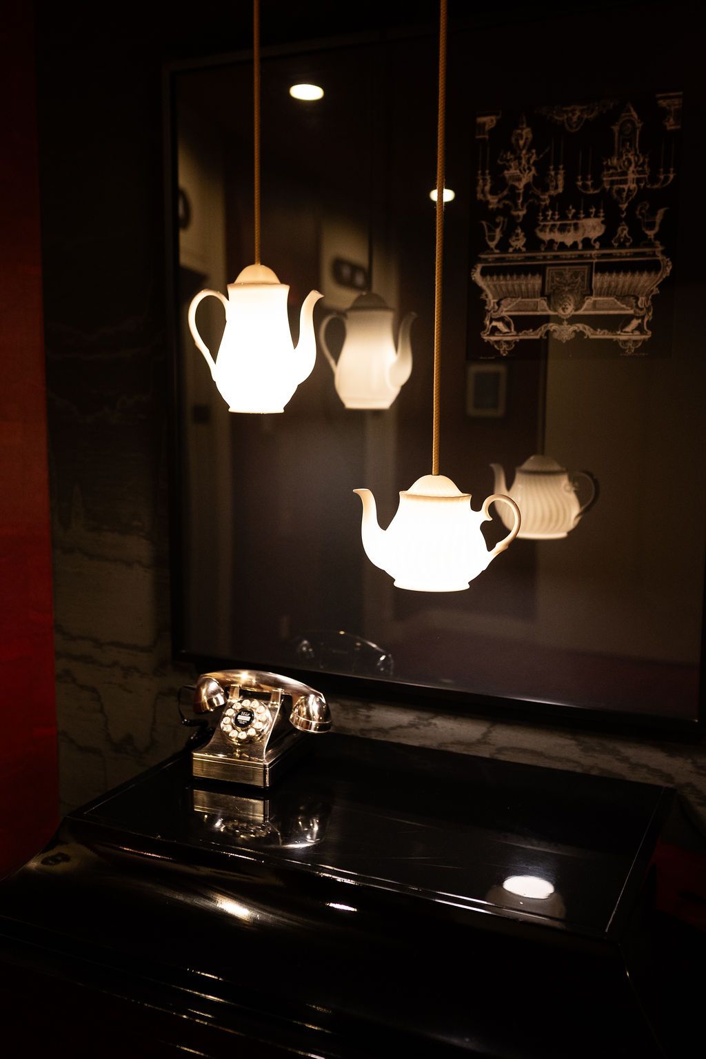 Unique teapot-shaped pendant lights hanging above a vintage telephone on a black marble dresser.