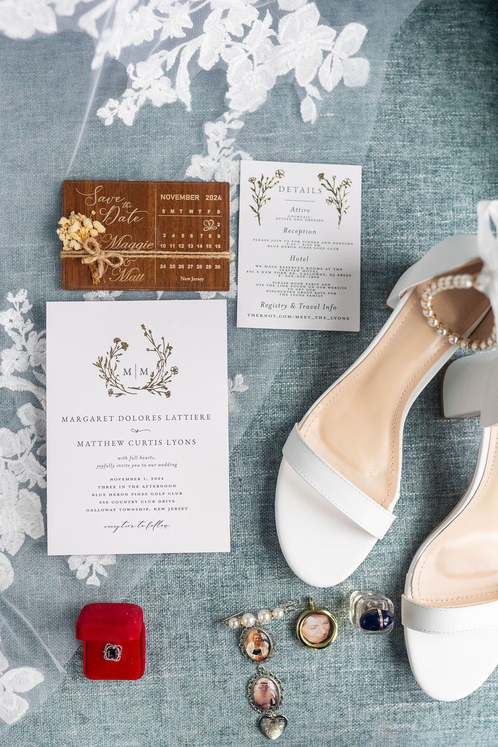 Elegant wedding flat lay with invitations, white pearl heeled sandals, jewelry, and a save the date card on blue linen.