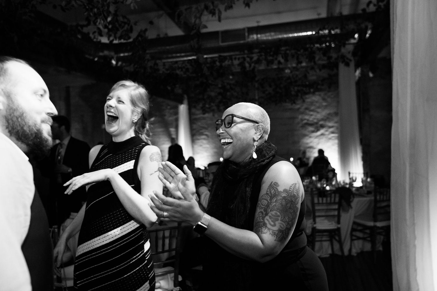 Guests laughing and clapping joyfully at a wedding reception in black and white photo.