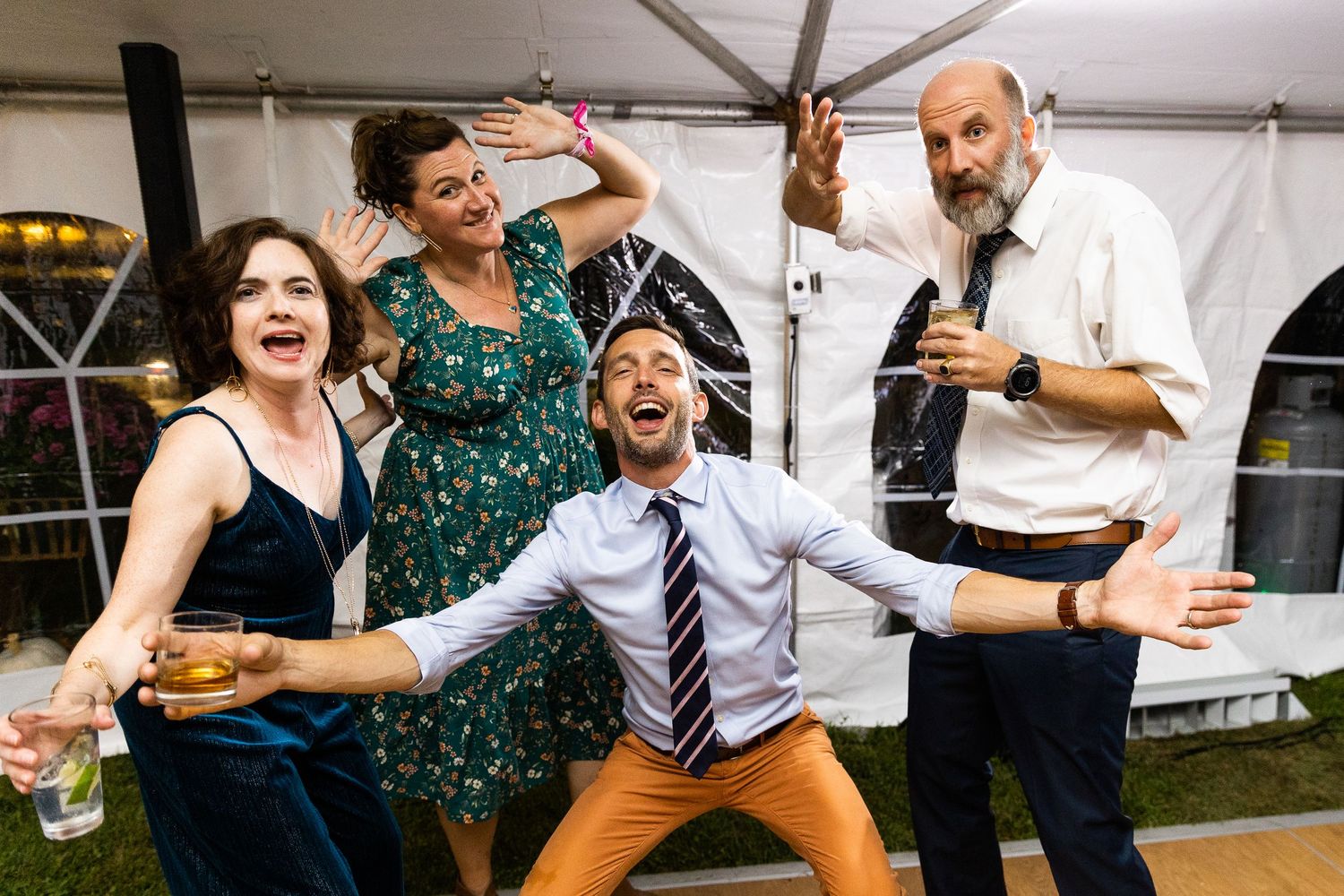 Four wedding guests laughing and posing dramatically together at an outdoor reception tent.