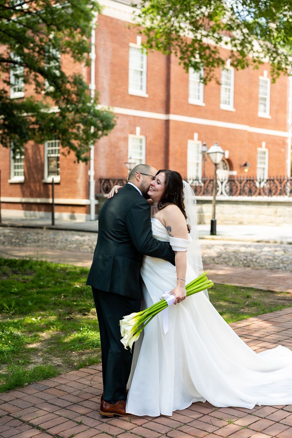 Bride and groom sharing a tender embrace and kiss outdoors near historic red brick building.