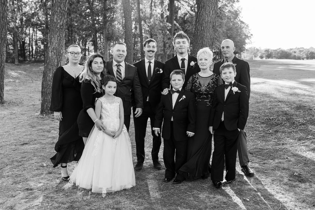 Black and white photo of a large wedding family group posing outdoors among tall pine trees.