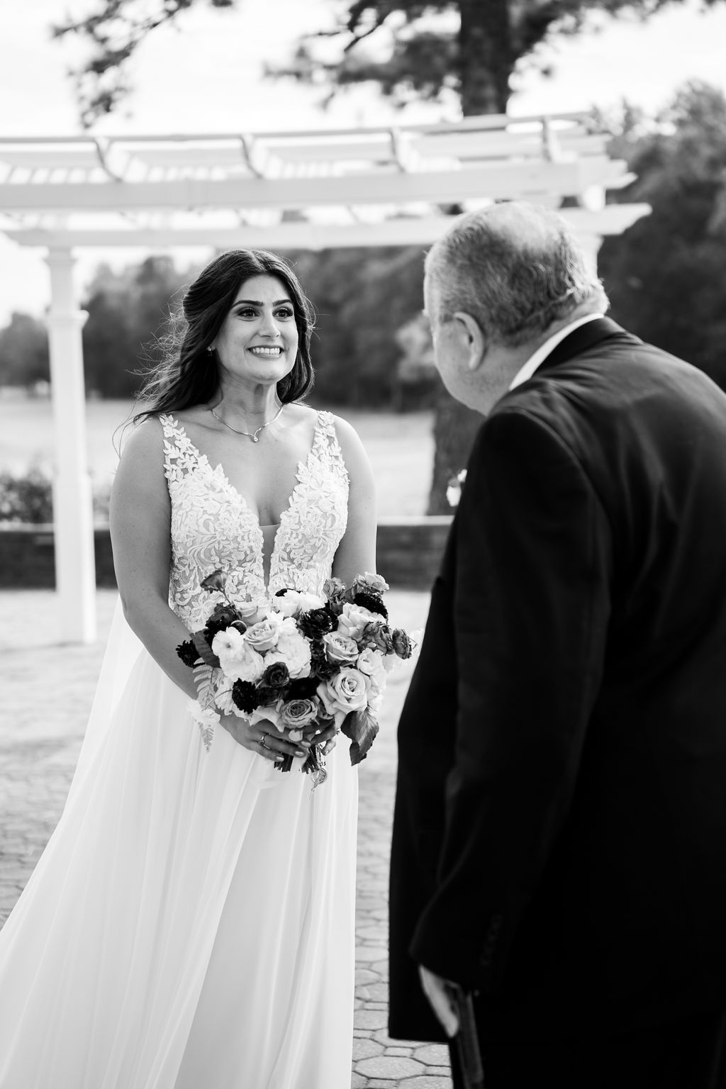 Radiant bride in lace gown smiling while holding bouquet during an outdoor first look moment.