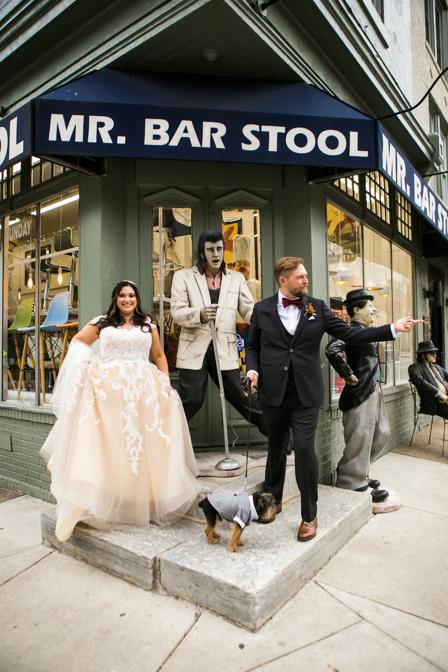 Bride and groom pose with Halloween street performers outside Mr. Bar Stool store with small dog.