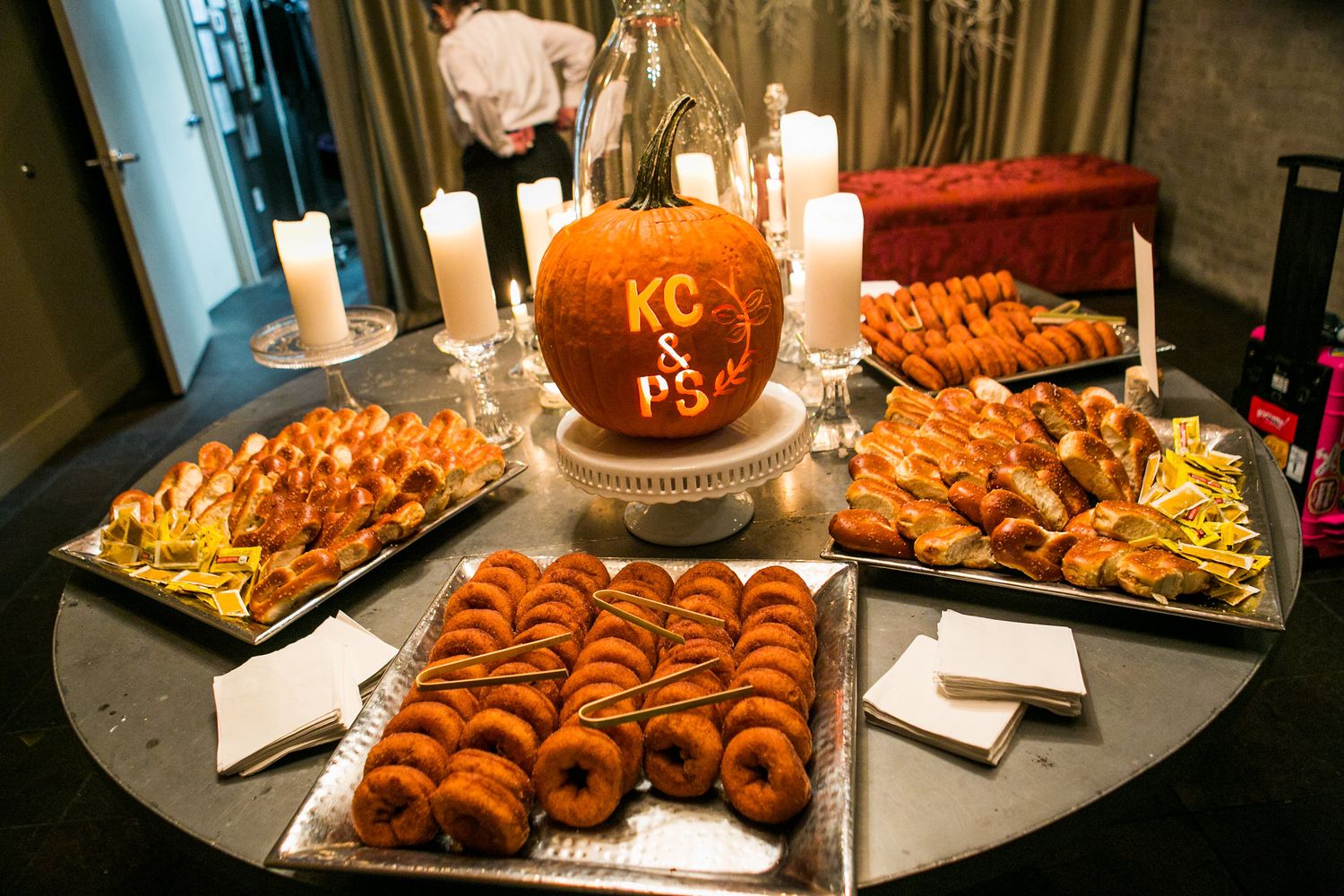 Halloween wedding snack table with carved pumpkin centerpiece displaying KC & PS initials, donuts, and pastries.