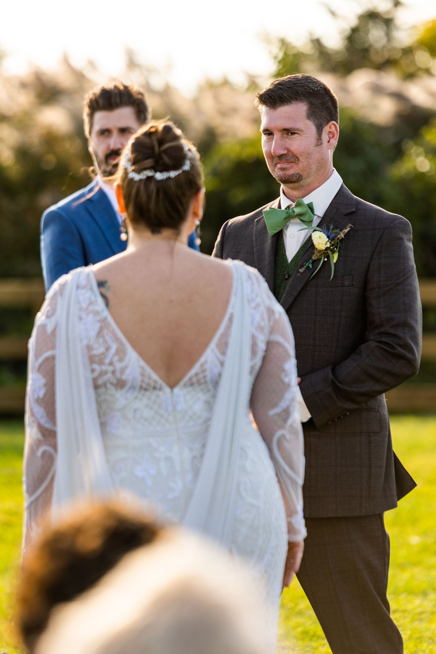 Emotional groom in plaid suit watches bride approach at golden hour outdoor wedding ceremony.